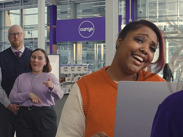 still from Currys 'Sigh of Relief' ad showing a customer speaking to a Currys member of staff over a laptop, with a BSL interpreter and audio describer present in the background